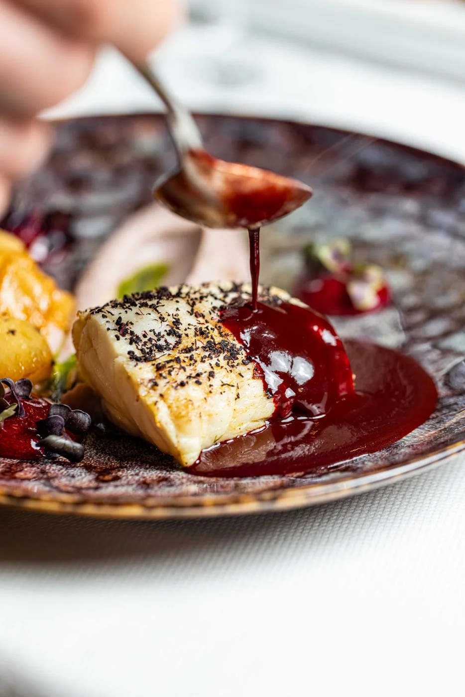Sauce being poured over a plated fish dish.