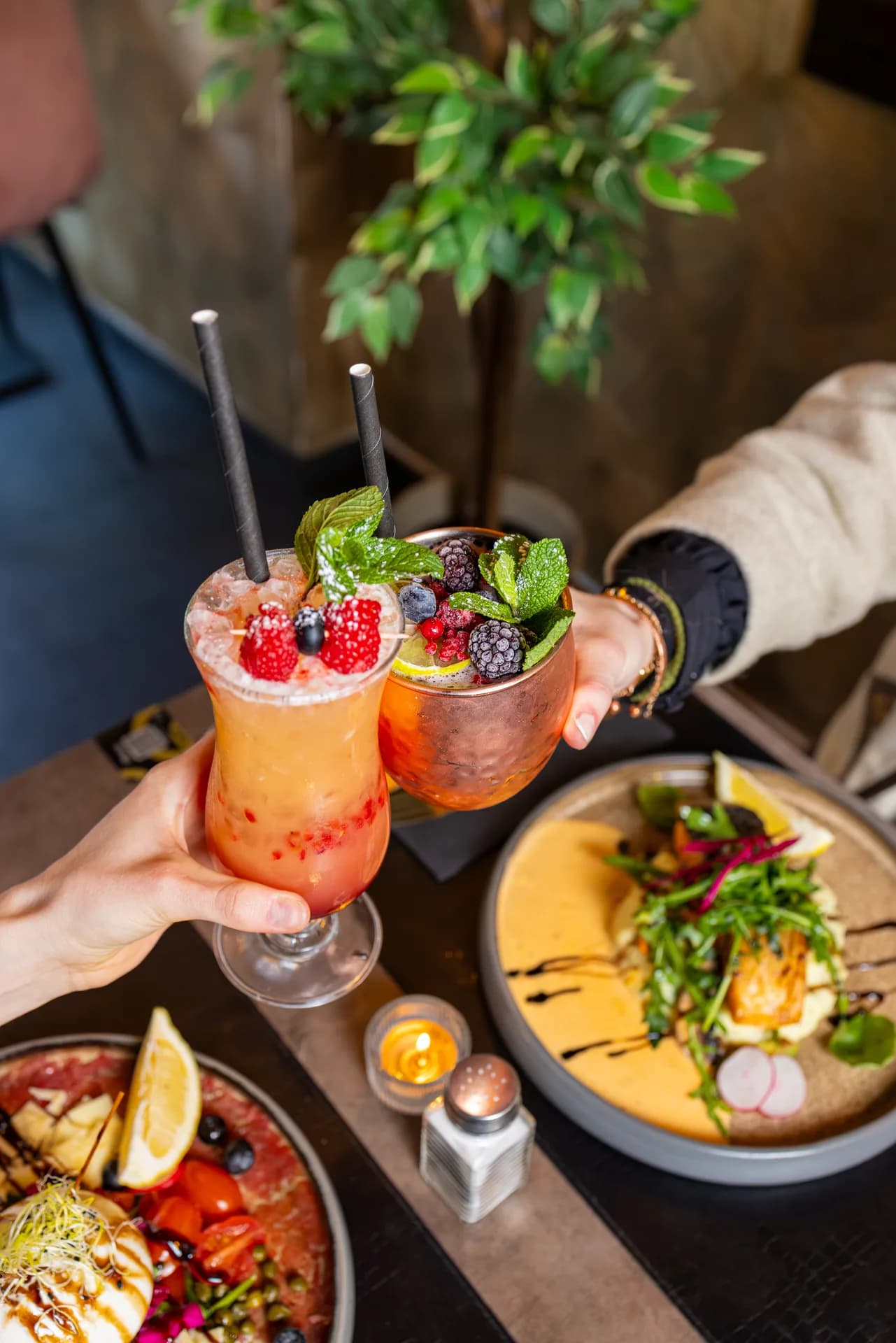 Hands serving colourful drinks and plated food for a content shoot.